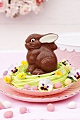 A chocolate Easter bunny in a nest decorated with flowers and chocolate eggs