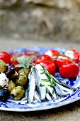 An antipasti platter with marinated anchovies, olives and pimientos filled with ricotta (Italy)
