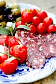 An antipasti platter with sliced salami, cherry tomatoes, pimientos filled with ricotta and olives