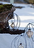 Aus Metallringen geformte Kugeln mit silberfarbenen Christbaumanhängern an Baumstamm im Schnee