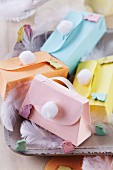 Colourful, spring-themes paper gift boxes shaped like handbags with handles and pompoms