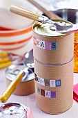 Food cans wrapped in brown paper and labelled with alphabet stickers