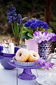 Doughnuts on a table outside decorated with crockery and blue and purple and flowers