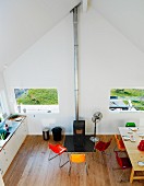 Blick von oben auf Küchenzeile, Essplatz mit bunten Schalenstühlen und den zwischen zwei Fenstern plazierten Schwedenofen