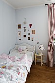 Kinderbett mit weißem Holzrahmen, daneben Nachttisch und rot-weiss gestreifter Vorhang