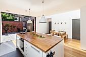 Kitchen island with wooden worksurface below retro pendant lamps; open folding doors leading to courtyard in background