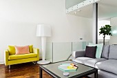 Loungebereich mit hellgrauem Couch, gelbem Polstersessel und Stehlampe im Designerstil