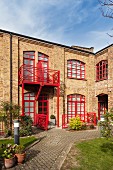 Former factory converted into residential building; red-painted window frames and balcony rails, courtyard with edged flowerbeds and paved paths