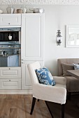 Comfortable dining area with simple, upholstered furnishings and floral scatter cushions in kitchen-dining room; reflections in oven door integrated into fitted cupboards