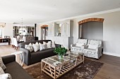 Open-plan interior in natural shades with brick lintel over arched doorway and tasteful sofas and armchairs around modern glass and wood table