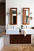 Twin sinks on masonry washstand with integrated cupboard below tall narrow mirrors on wall