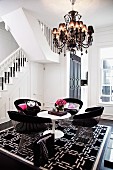 Klassiker Armlehnstühle aus Metalllamellen und weisser Tulip Table auf schwarzweiss gemustertem Teppich unter Kronleuchter und Treppenaufgang