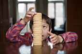 A boy stacking biscuits on a table