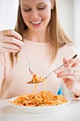 A young woman eating fettuccine with tomato sauce