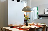 Dining table set with striped beakers and vase of flowers below pendant lamp in dining room