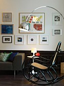 Retro Bogenlampe über Thonet Schaukelstuhl, im Hintergrund Tulip Table und Couch, vor Wand mit Bildersammlung über Holzwand