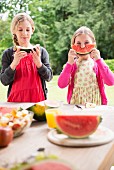 Zwei Schwestern essen und halten Wassermelonenscheiben auf der Terrasse