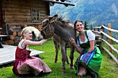 Zwei Frauen im Dirndl und ein Esel vor einer Hütte
