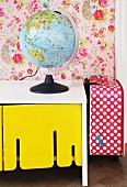 Globe lamp on white, retro sideboard with yellow-painted cupboard doors and red and white polka-dot suitcase to one side