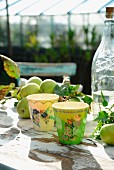 Bemalte Bechern, Apfelzweig und und Vintage Limonadenflasche auf rustikalem Tisch im Garten