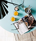 Open cookbook, glasses of juice and palm frond on ice-blue tabletop