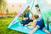 Young couple and toddler daughter having a tea party in tent