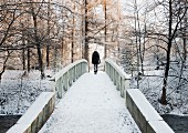 Rückenansicht einer Frau die eine schneebedeckte Brücke überquert