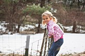 Young girl climbing wire fence in field