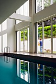 Indoor pool in contemporary house with double-height glass facade and view of garden