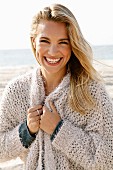 A young blonde woman by the sea wearing a beige cardigan