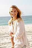 A young blonde woman by the sea wearing a white woollen jumper