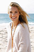 A young blonde woman by the sea wearing a white woollen jumper