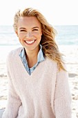 A young blonde woman by the sea wearing a denim shirt and a white woollen jumper