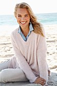 A young blonde woman by the sea wearing a denim shirt and a white woollen jumper