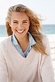 A young blonde woman by the sea wearing a denim shirt and a white woollen jumper