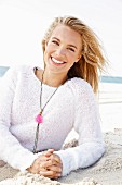 A young blonde woman by the sea wearing a light knitted jumper