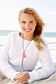 A young blonde woman by the sea wearing a light knitted jumper