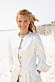 A young blonde woman on a beach wearing a white coat