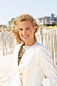 A young blonde woman on a beach wearing a white coat