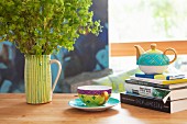 Teacup next to teapot on stack of books and ceramic jug of lady's mantle