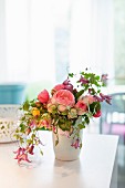 Bouquet of fragrant English roses, clematis and other flowers in white vase on table