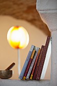 Row of books and singing bowl and striker on masonry surface with standard lamp in background