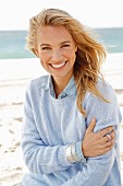 A young blonde woman by the sea wearing a blue knitted jumper and a denim shirt