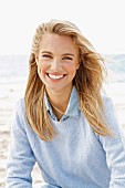 Junge, blonde Frau in blauem Strickpullover und Jeanshemd am Meer