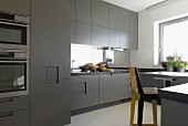 Minimalist kitchen with grey doors; wooden bar stool in foreground