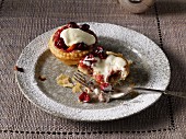 Two cranberry tartlets on a plate with cream, one half eaten