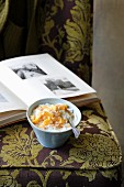 Coconut rice pudding with mango on an upholstered chair in front of a photo album