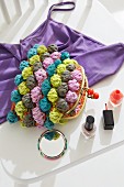 A purse with colourful bobbles next to a small mirror and bottles of nail varnish