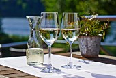 Two glasses of white wine and a carafe on a sunny terrace table