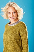 A young blonde woman wearing an olive-green knitted jumper